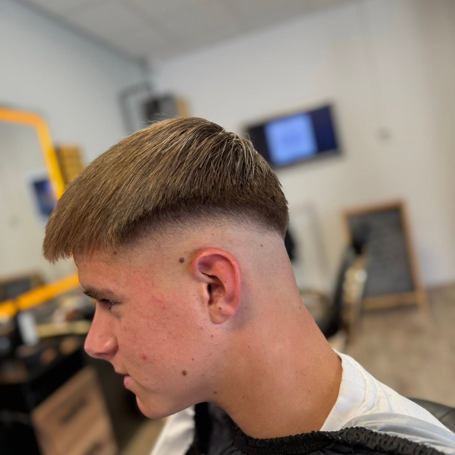 Zijaanzicht van een jonge klant met een crop en een skin fade, in de zaak met verlichte spiegels