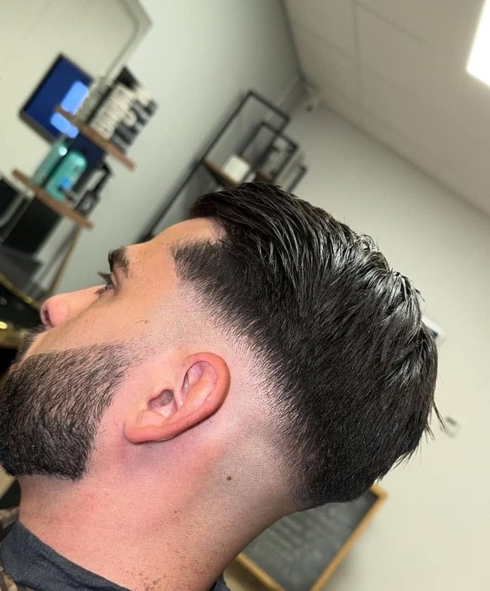 Zijaanzicht van een klant met achterover gekamd haar, een fade in de nek en een strak bijgewerkte baard