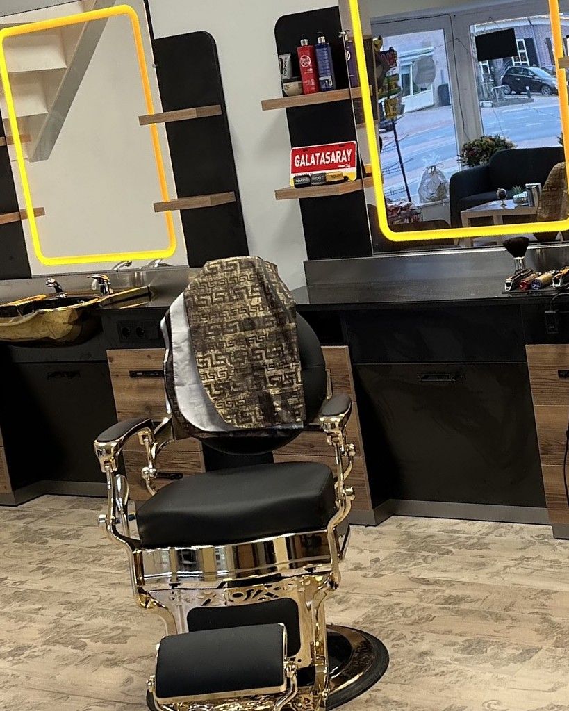 Een zwart-gouden barberstoel voor een verlichte spiegel in de zaak
